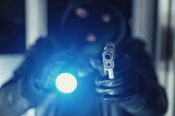 Burglar or a thief holding a gun with flashlight in a house