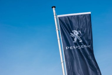 AACHEN, GERMANY MARCH, 2017: Peugeot logo on a flag against blue sky. Peugeot is a French cars brand, part of PSA Peugeot Citroen. clipart