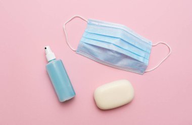 Mavi tıbbi maske, pembe arka planda sabun ve el dezenfektanı. Corona virüsü covid 19 salgınına karşı koruma kavramı.