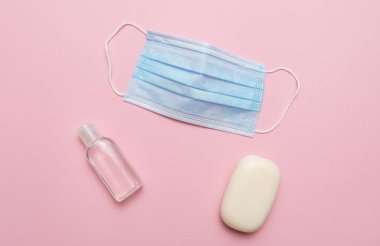Mavi tıbbi maske, pembe arka planda sabun ve akıcı sabun. Corona virüsü covid 19 salgınına karşı koruma kavramı.