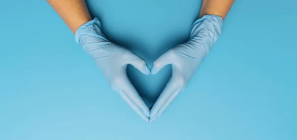 Thanks you doctors in the Corona pandemic, horizontal banner with copy space for text. Female hands in blue gloves show symbol of heart shape on blue background.