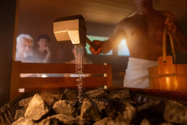 Człowiek Trzymający Drewniane Wiadro Wylewający Wodę Gorące Kamienie Łyżką Deszczu — Zdjęcie stockowe
