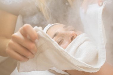 Gözü kapalı bir kadının yüzüne kozmetoloji salonu ya da spa salonunda havluyla termal buhar tedavisi yaptırırken.. 