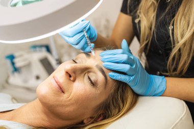 Genç bir kadın alnına yaşlanmayı önleyici yüz tedavisi yaptırıyor. Güzellik salonundaki kadın. Plastik cerrahi kliniği.