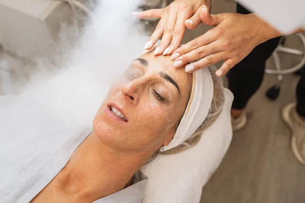 Beauty treatment of a woman with ozone facial steamer and cream massage in the face