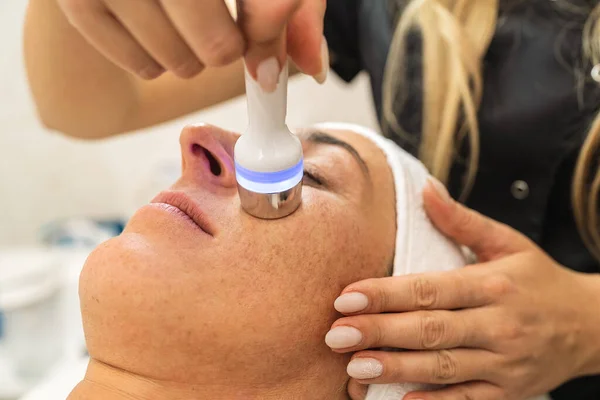 Side view of woman receiving hydrafacial therapy on forehead at beauty spa or cosmetology salon.