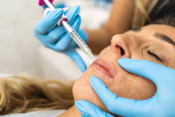 The doctor cosmetologist makes Lip augmentation procedure of a beautiful woman in a beauty salon. Cosmetology skin care.