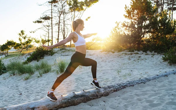 Genç bir kadın sabahları sahilde ağaç gövdesinde yoga yapıyor.