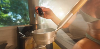 Norveç 'te ahşap varil saunasında mala suyu damlatan bir şişeden gerekli aromatik yağı damlatıyor. Buhar, spa ve sağlık konsepti, rahatlatıcı ve tatilin tadını çıkarın.
