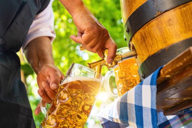 Önlüklü Bavyeralı adam bira bahçesindeki ahşap bira fıçısından bira dolduruyor. Oktoberfest, halk ve bira festivali için arka plan (Almanca: Ozapft)!) 