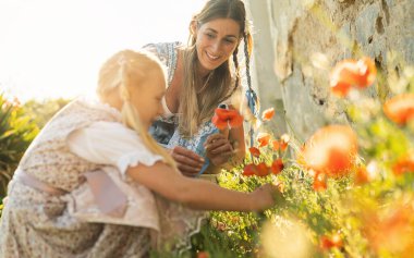 Sweet little girl and her mother in traditional bavarian tracht picking poppies plants outdoor in a village at oktoberfest clipart