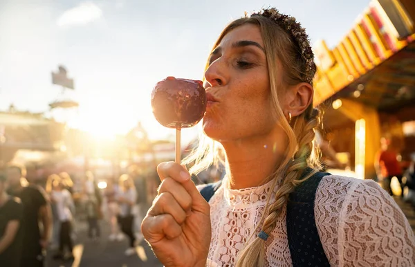 Woman eating candy apple at Oktoberfest wearing Dirndl in germany