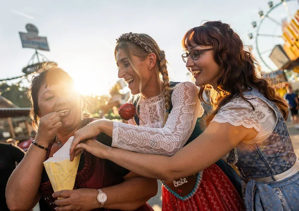 Friends eat roasted almonds together from the paper bag in front of the gingerbread stand at a Bavarian fair or oktoberfest or duld in national costume or Dirndl