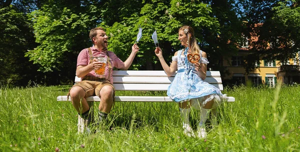 Young man and woman sitting on a bench throw away their masks for Social distancing and corona protection in Bavarian beer garden or oktoberfest