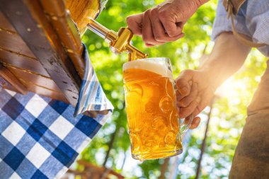 Deri pantolonlu Bavyeralı adam bira bahçesindeki ahşap bira fıçısından fıçıya bira dolduruyor. Oktoberfest, halk ve bira festivali için arka plan (Almanca: Ozapft)!) 