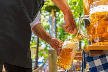 Önlüklü Bavyeralı adam bira bahçesindeki ahşap bira fıçısından bira fıçısına bira dolduruyor. Ekim Festivali ya da Withe, halk ya da bira festivali için arka plan