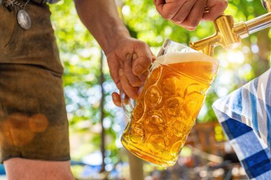 Deri pantolonlu Bavyeralı adam bira bahçesindeki ahşap bira fıçısından fıçıya bira dolduruyor. Oktoberfest, halk ve bira festivali için arka plan (Almanca: Ozapft)!) 