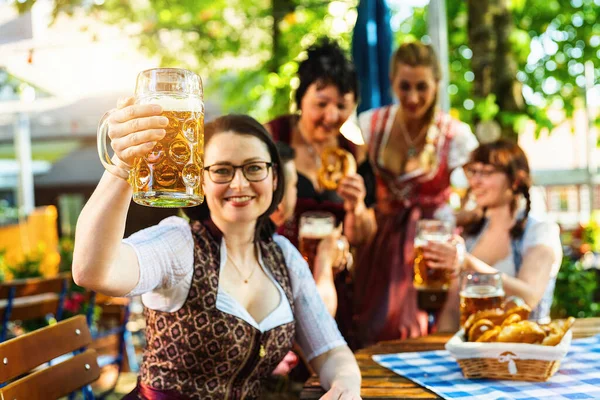 Arkadaşlar, iki erkek, üç kadın, bira bahçesinde ayakta ve oturuyorlar ya da bira bardaklarıyla Ekim Festivali
