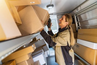 Bir müşteriye teslim etmek için minibüsündeki paketleri arayan kadın teslimatçı.