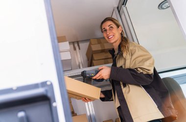 Kadın teslimatçı barkodu tarıyor. Kamyonetinde barkod tarayıcısı var.