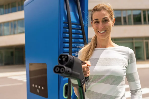 Beautiful woman holding a DC CCS2 EV charging connector on a Hypercharger or Supercharger for recharge her car.