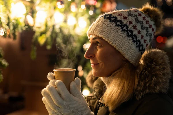 冬の市場でクリスマスツリーの前の女性ホットワインを飲む — ストック写真
