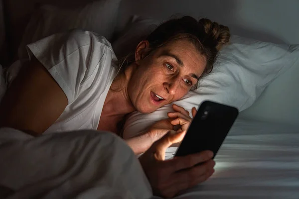 여자는 밤늦게 침대에서 스마트폰을 합니다 온라인 데이트 사진을 사람은 어두운 — 스톡 사진