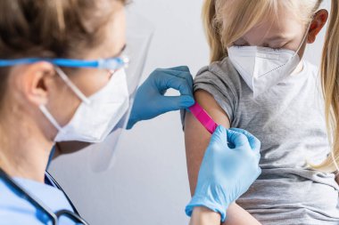 Koruyucu eldivenli doktor koluna yapışkan bandaj yapıştırıyor. Sarışın bir kızın koluna. Kovid 19 koronavirüs aşısı olduktan sonra..