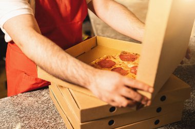 Pizza fırıncısı İtalyan pizzacıda paket servis için salamlı pizza paketliyor.