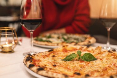 İnsanlar İtalyan restoranında kırmızı şarap içip fesleğenli margherita pizza yiyorlar.