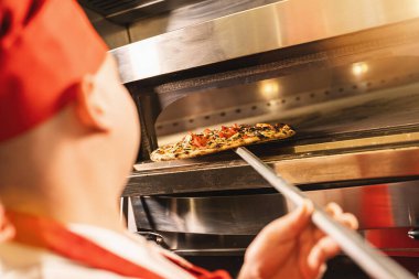 Erkek aşçı İtalyan pizzacıdaki taş fırından bitmiş pizzayı çıkarır.