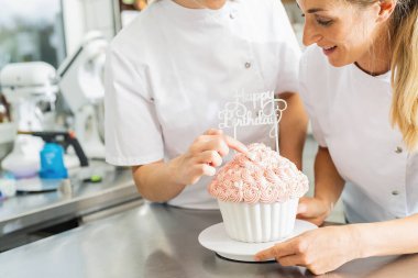 Pasta fırınında büyük doğum günü pastasını şekerle süsleyen şekerlemeciler.