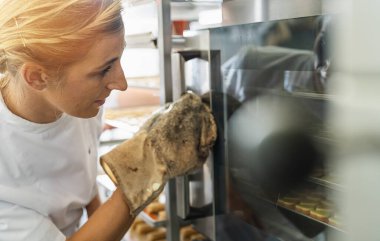 Fırındaki mutlu fırıncı kadın fırındaki cam kapılarla fırını kontrol ediyor.