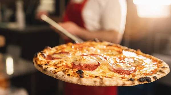 stock image Restaurant chef takes salami pizza from oven. Preparing traditional italian pizza. chef holding shovel with cooked Italian pizza from a wood-fired oven.