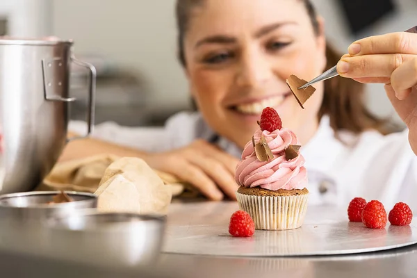 stock image happy women in pastry bakery as confectioner draped pieces of chocolate on a muffin topping with tweezers