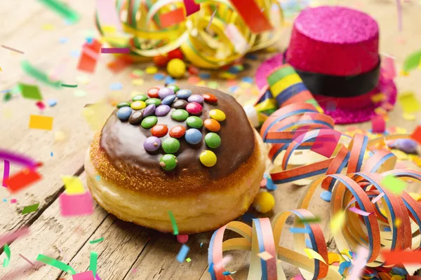 stock image Krapfen, berliner or Carnival donut from Germany with icing sugar on a light wooden surface with confetti and streamers on it - background for a carnival party or parties