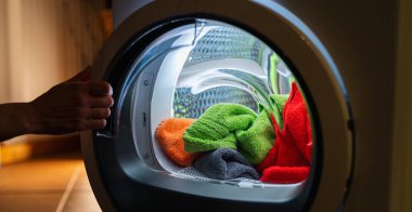 Housewife opens a  washing machine or dryer at night with many colorful clean fresh hand towels clipart
