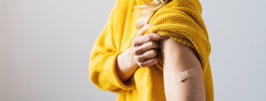 Corona COVID-19 ve SARS Cov aşısı. Kadın süveterinin kolunu kaldırıyor ve kolunu yapıştırıcı bandajla gösteriyor. Aşı olduktan sonra sıva, metin için kopyalanma alanı, pankart boyutu...