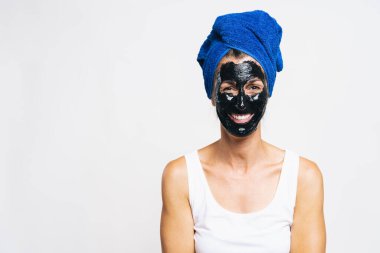 Yüzünde arındırıcı siyah maske ve kafasında banyo havlusu olan bir kadın. 