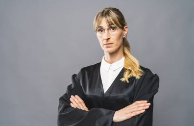 Kadın avukat, kollarını kavuşturmuş gri bir duvardaki mahkeme salonundaki kameraya bakıyor. Hukuk ve adalet kavramı imajı