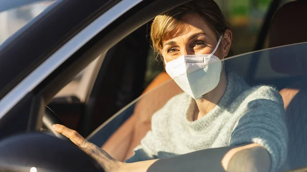 Beautiful woman with a N95 FFP2 anti virus mask sitting in a car, protective mask against coronavirus, driver on a city street during a coronavirus outbreak, covid-19.