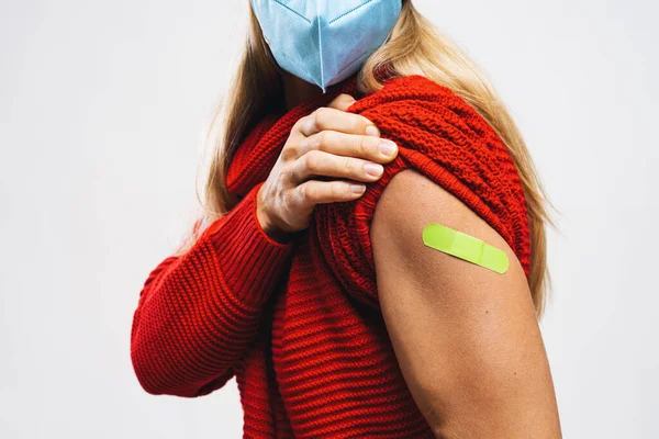 vaccine injection for corona virus COVID-19. Woman with face mask holding up her sweater sleeve and showing her arm with green Adhesive bandage Plaster after receiving vaccination