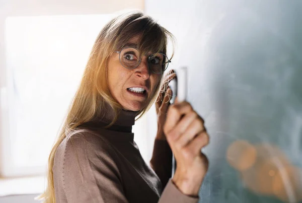 Angry teacher in glasses with Chalk in hand in front of a blackboard