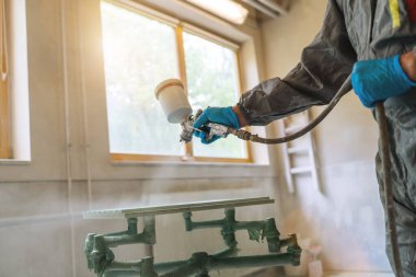 Marangozluk atölyesindeki ahşap paneli boyamak için sprey tabanca kullanan koruyucu kıyafetli biri.