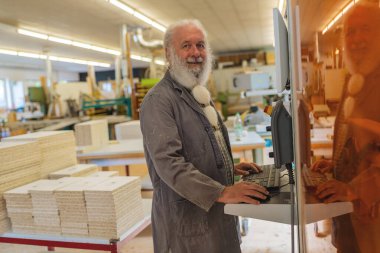 Marangozluk atölyesinde kesim makinesi kullanan gülümseyen sakallı bir adam.