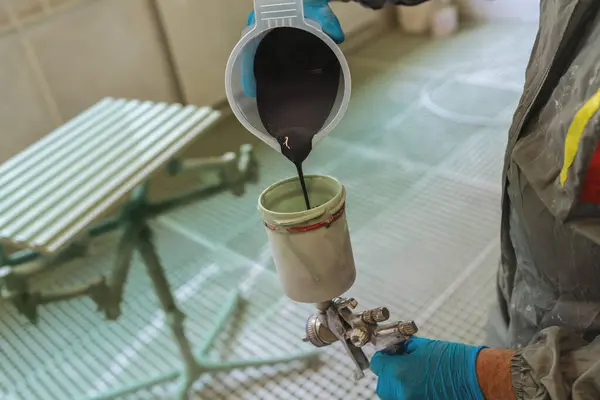 Filling a paint sprayer with dark gray paint in a preparation for painting a wooden panel