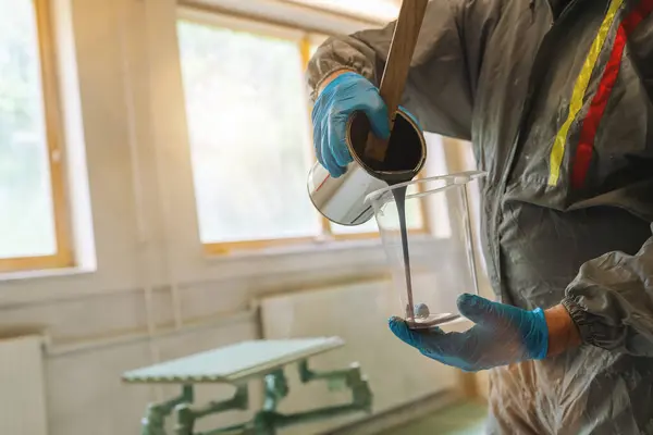 Person in protective suit pouring paint into a measuring cup in wood factory
