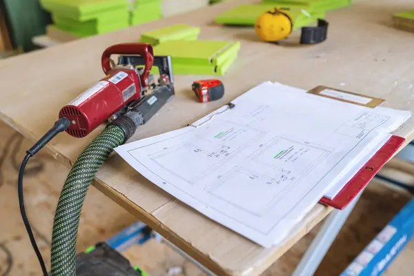 Electric saw and architectural plans on a workbench with a tape measure