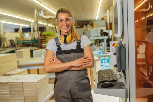 Confident woman with crossed arms and hearing protection in a carpentry workshop