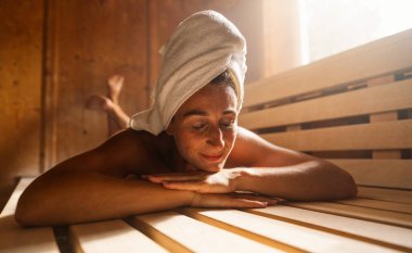 Finnish sauna tezgahında uzanmış kafasında bir havluyla tatmin olmuş bir kadın. Spa Sağlık Oteli konsept görüntüsü.